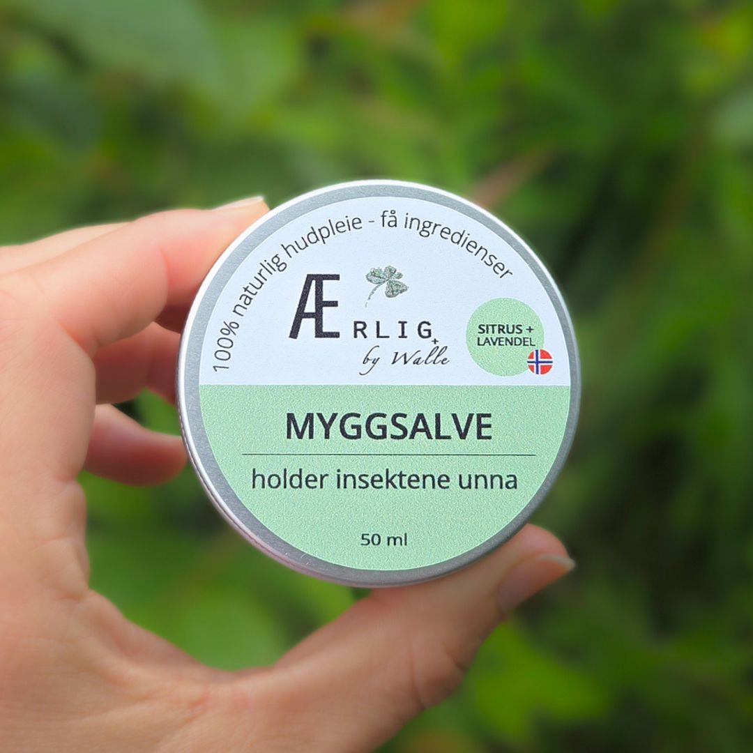 Myggsalve fra ærlig by walle holdes av hånd mot kamera, natur i bakgrunnen