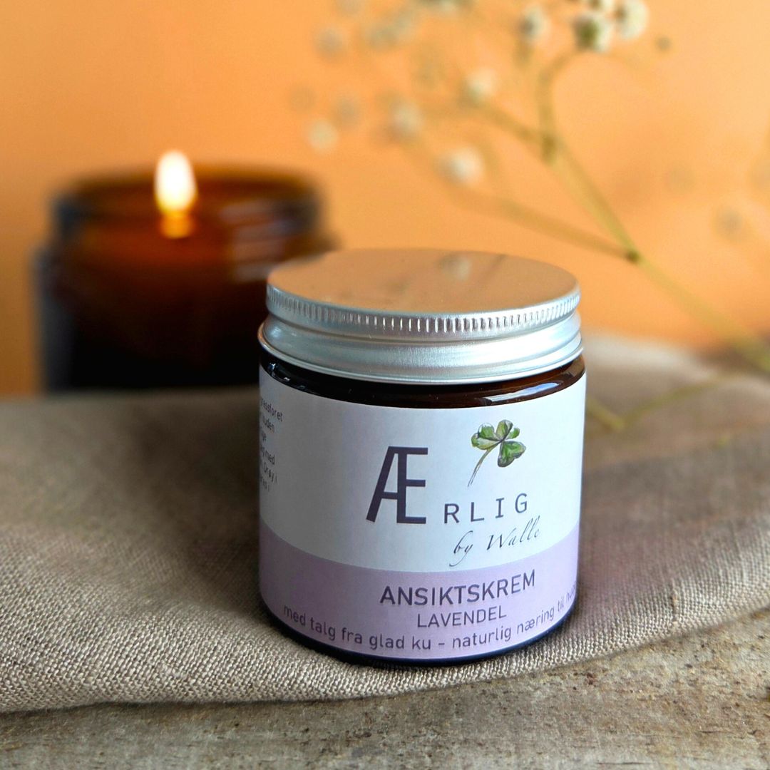 ansiktskrem lavendel fra ærlig by walle på mykt stoff foran levende lys og blomster