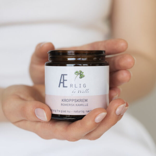 Hender holder frem Kroppskrem med romersk kamille fra Ærlig by Walle, talgbasert
