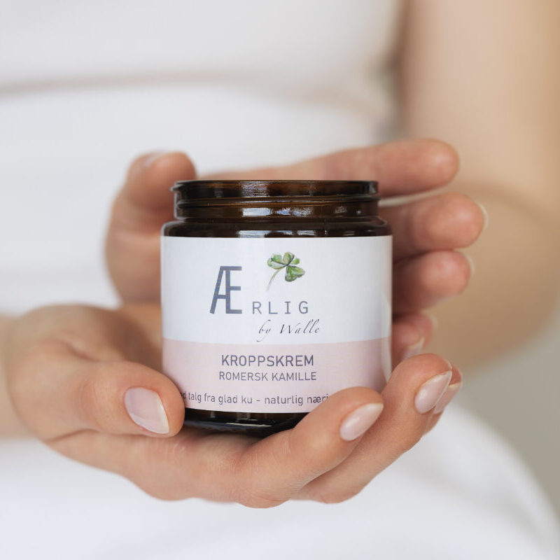 Hender holder frem Kroppskrem med romersk kamille fra Ærlig by Walle, talgbasert