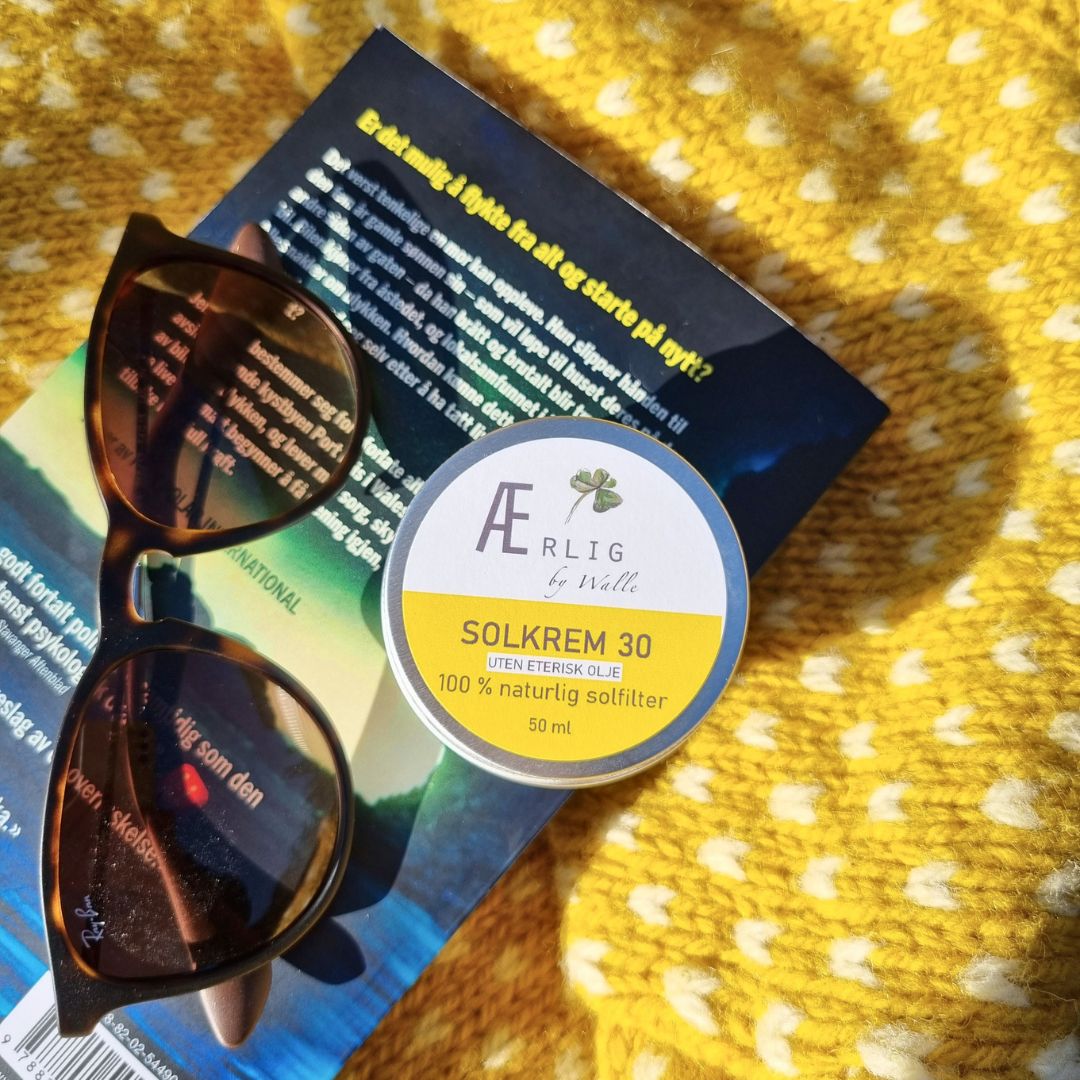 påskestemning, solkrem fra ærlig by walle ligger på gul genser, med bok og solbriller