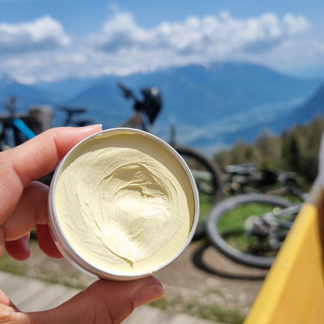 åpen krukke med lyd gul krem holdes mot kamera, sykler og utsikt i bakgrunn